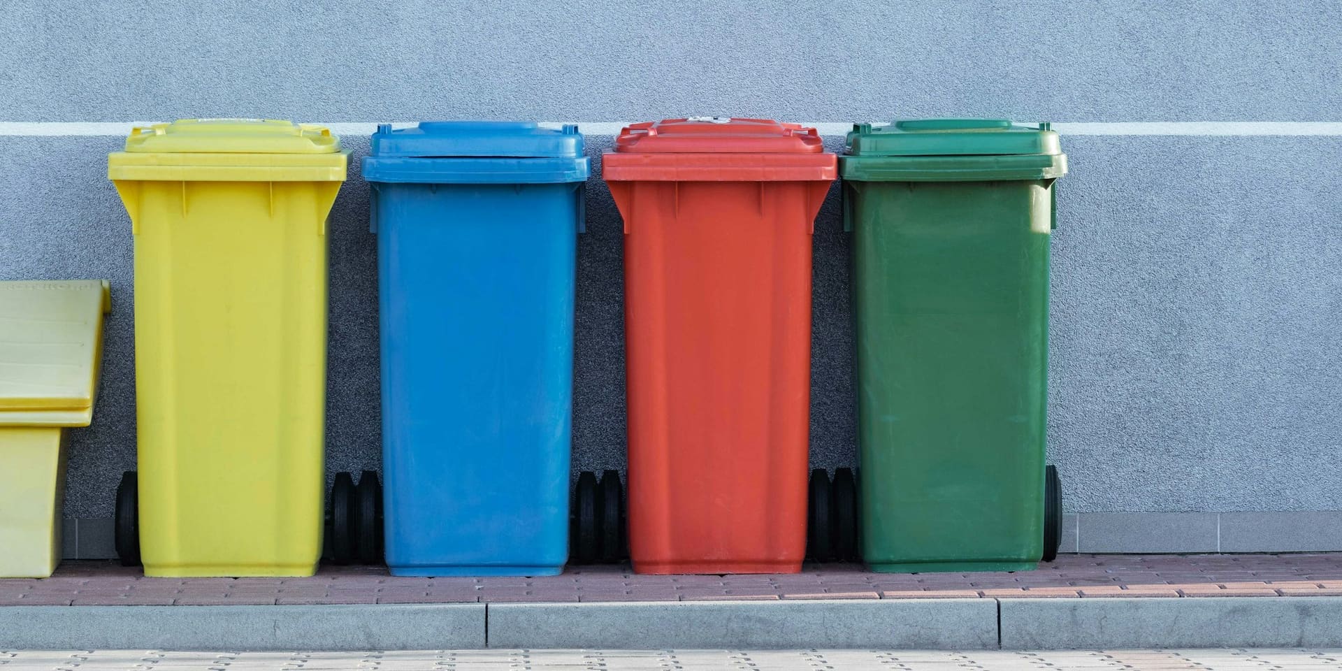 Contenedores de reciclaje de colores alineados junto a un muro